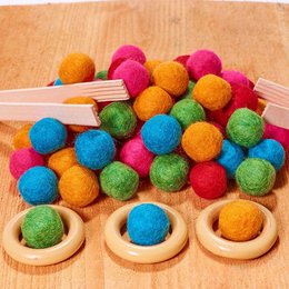  Colorful felt balls in various sizes and shapes, including round and oval, in a wooden tray. The balls are in vibrant shades of pink, orange, green, and blue, creating a visually appealing sensory toy.