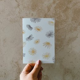 Postcard with a pattern of daisies printed on recycled paper. The postcard features a variety of daisy shapes and sizes in shades of gray and yellow against a white background.