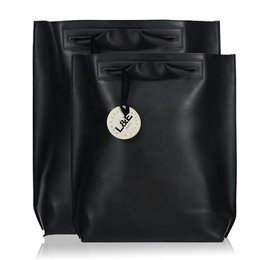  A medium-sized backpack made of grainy or lightweight vegetarian leather, available in a variety of colors including black, deep red, taupe, sky blue, gunpowder, light grey, navy, plum, tan, deep forest, papaya, and bourbon. The backpack features a simple, minimalist design with a round metal charm.