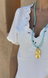 A long turquoise necklace with a delicate lace pattern and a small pendant charm.