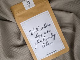 A tall, round candle in a beige paper package with handwritten text that says "Well behaved women seldom make history."