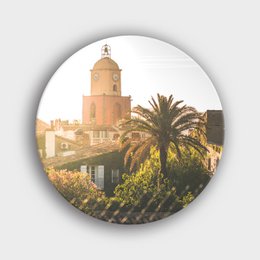 A circular wall decor featuring a Mediterranean town with a bell tower and palm trees in the foreground.