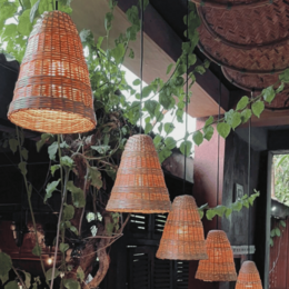 A woven, bell-shaped lamp shade made of natural materials. The shade has a simple, minimalist design that would complement a variety of interior styles.