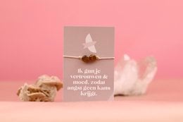 A beaded bracelet with the words "Proud - trust and courage" printed on a tag. The bracelet features a white feather charm, symbolizing trust and courage.