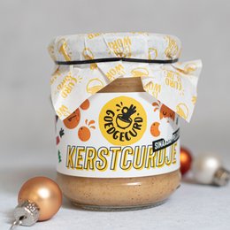 A festive jar of Christmas-themed spread, featuring a whimsical design with holiday motifs like stars and snowflakes. The product is labeled "Kerstcurdje," indicating it is a seasonal Christmas-themed spread.