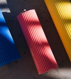 Tall, cylindrical pillar candle in a variety of vibrant colors including pink, yellow, and blue. The candle has a ribbed texture and a simple, modern design.
