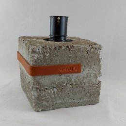 A raw, industrial-style concrete garden torch in multiple colors including black and cognac. The torch has a square, blocky shape with a textured concrete surface.