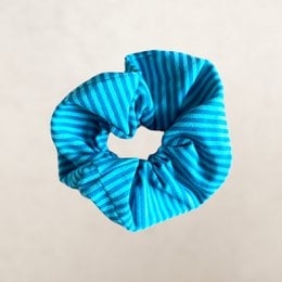 A light blue scrunchie with a pleated, textured design. The scrunchie has a soft, stretchy fabric that would be comfortable to wear in the hair.