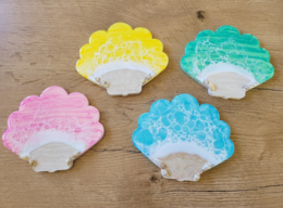 "Colorful shell-shaped coasters in pastel shades of yellow, pink, and blue. The coasters feature a textured, lace-like pattern that adds a decorative touch to any table setting."
