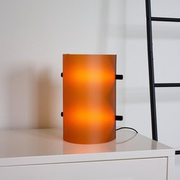 Tall, cylindrical table lamp with an amber-colored glass shade, providing a warm, ambient lighting for a modern interior.