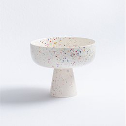  A round, white ceramic bowl with a pedestal base, featuring a speckled pattern of colorful dots throughout.