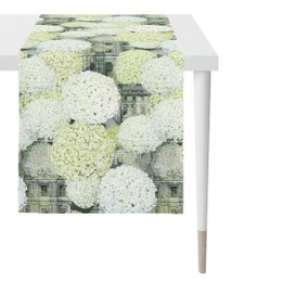 A long, rectangular table runner featuring a pattern of white hydrangea flowers against a green and gray background. The runner is suitable for use on a dining table or other indoor or outdoor surfaces.