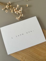  A simple, elegant white card with the text "I love you" printed on it, accompanied by a bouquet of dried flowers.