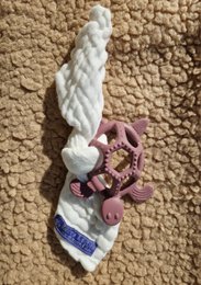 A white twisted teething ring with a purple and white cloth attached, designed for babies to chew on and soothe their gums during the teething process.