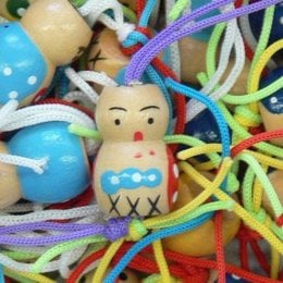 Colorful assortment of wooden dolls and toys, including a smiling doll with a painted face and surrounded by vibrant strings and shapes.