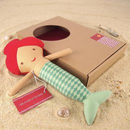 A plush mermaid doll with a black body, pink and white patterned tail, and a smiling face.
