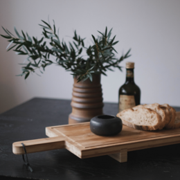 A round, dark-colored ceramic salt jar with a simple, minimalist design. The jar has a smooth, glossy finish and a small opening at the top for dispensing salt.