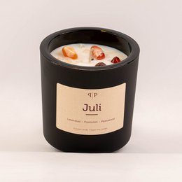 Gemstone scented candle in a black container with a label that says "Juli". The candle has a round, tall shape and appears to be made of wax with visible gemstones or crystals embedded in it.