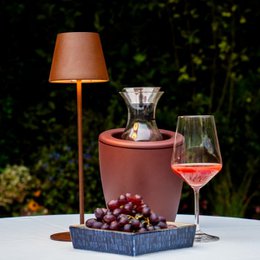 A round, tall wine and champagne cooler with gel bags in dark cherry, venice blue, and sage green colors. The cooler has a lamp-like design and is shown with a glass of wine and grapes.