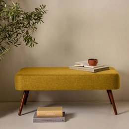 A mustard yellow or red upholstered bench with wooden legs, suitable for seating 1-2 people.