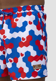 Colorful patterned men's swim trunks in a bold hexagon design featuring shades of red, white, and blue.