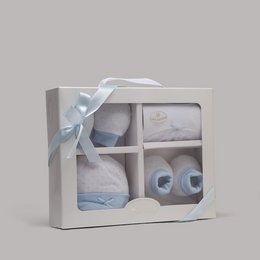 A set of 4 baby accessories including a hat, gloves, bib, and socks in a light blue color palette. The items are presented in a gift box with a ribbon.