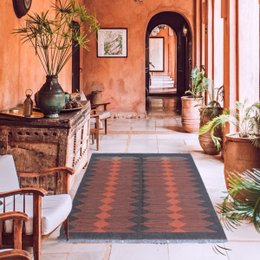 A modern, raspberry-colored kilim rug with a geometric diamond pattern, suitable for use as a runner in a hallway or entryway.