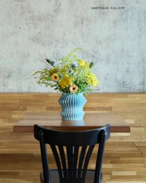  Tall, cylindrical vase in light blue color with a vibrant floral arrangement featuring yellow, orange, and green flowers.