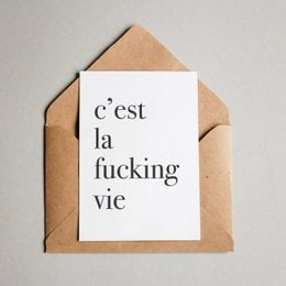 A card with the text "C'est la fucking vie" printed on it, enclosed in a beige envelope.