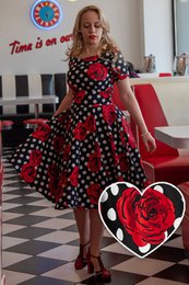  A 50s style swing dress in a rose polka dot pattern, featuring a fitted bodice and a flared skirt. The dress has a retro, feminine aesthetic.