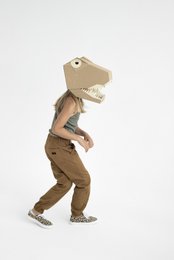 A cardboard T-Rex mask with a large open mouth and teeth, worn by a person in a beige outfit.