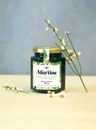 A jar of Linden honey with a green label and a sprig of white flowers. The honey appears to be a light golden color.