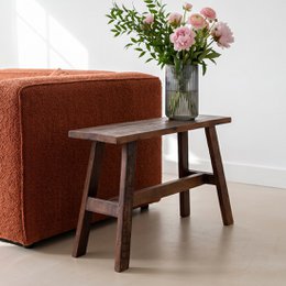 A large, rustic wooden bench with a simple, minimalist design. The bench features a solid wood top and a sturdy, angled wooden frame in a dark, rich brown color.