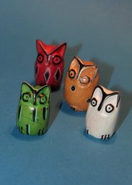 Colorful soapstone owl statues in various shades of red, green, and brown. The owls have distinct facial features and shapes, making them unique decorative pieces.