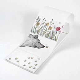A notepad with a whimsical illustration of bees and flowers on the cover. The notepad has a soft, textured surface and a trio of floral designs.