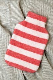 Striped hot water bottle cover in tomato red and off-white colors. Made of soft, cozy material for keeping warm.