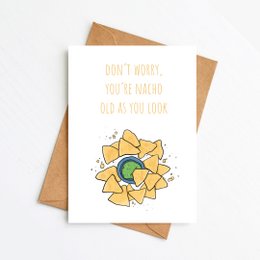 A birthday card with a playful design featuring a sunflower-like shape made of nacho chips and the text "Don't worry, you're nacho old as you look".