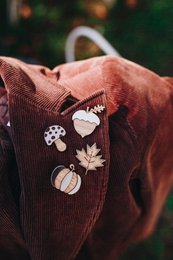  Wooden autumn pins in the shape of a mushroom, leaf, pumpkin, and hazelnut on a checkered fabric background.