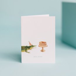 A whimsical greeting card featuring a party animal alligator and a celebratory cake on a pedestal, perfect for a birthday or other festive occasion.
