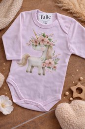 Lavender purple baby bodysuit with cute unicorn illustration surrounded by pastel flowers and floral wreath design.
