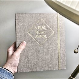 A pregnancy journal with a linen-textured cover and a spiral binding. The journal includes various sections and pages for tracking pregnancy milestones, notes, and other information.