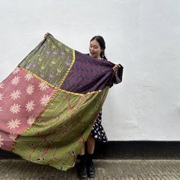 A large, colorful, patterned shawl or scarf in shades of green, pink, and purple with floral designs. The shawl appears to be made of a lightweight, flowing material and is being held up by a person in the image.