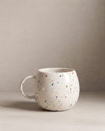  A white ceramic mug with a speckled pattern, featuring a round, tall shape and a handle. The mug is suitable for parties and events.