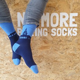Navy blue and light blue patterned socks with the text "No more boring socks" on a wooden background.