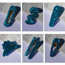 Glittery teal resin hair clips in various shapes and sizes, including a heart, crescent moon, and abstract designs.