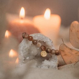 Beaded bracelet with natural stone beads and a gold-colored charm. Warm, earthy tones and a calming, spiritual aesthetic.