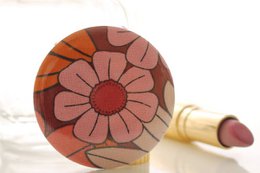 Compact makeup mirror with a floral design in shades of orange, red, and pink. The mirror has a round shape and a decorative pattern.