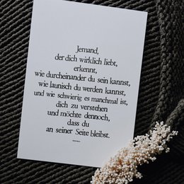 A black and white art print featuring a German poem with the title "Jemand, der dich liebt" (Someone who loves you). The poem appears to be handwritten or printed in a cursive font on a plain white background.