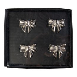  Set of 4 silver-colored napkin rings in the shape of bows. Each napkin ring measures approximately 5x4.5cm.