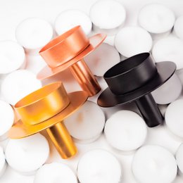 A set of 60 black, gold, and rose gold tea light holders. The holders have a simple, modern design and are suitable for use with tea light candles.